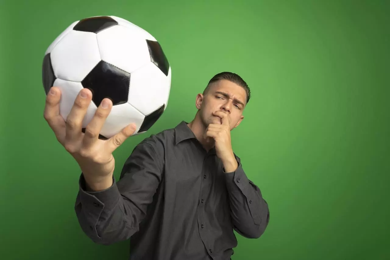 Homme réfléchi tenant un ballon de football, symbolisant la psychologie des paris sportifs